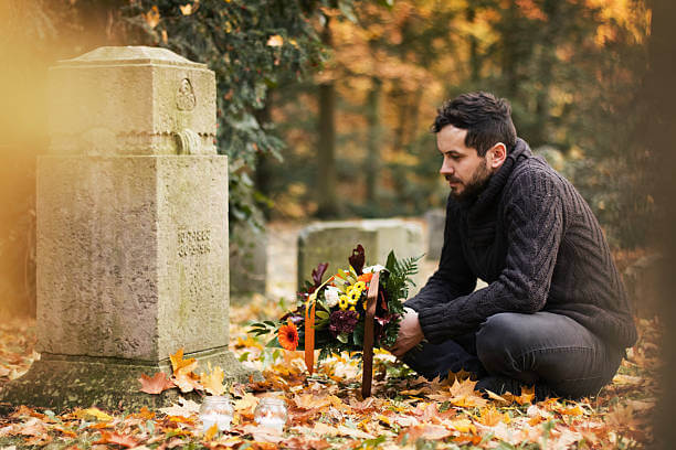 Mid adult man with flowers and candles visiting graves at the cemetery.